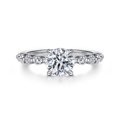Like a masterpiece of light and elegance, this engagement ring features a single-prong setting crafted to cradle a dazzling 1-carat round-cut diamond. The 14K white gold band, kissed with a trail of smaller diamonds that gracefully encircle it halfway, offers a hint of starlight with every movement, telling its own love story.